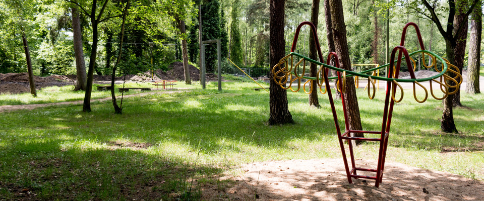 Spielplatz am Mobilheimplatz Entenfangsee, umgeben von Bäumen, mit einem runden Metallklettergerüst im Vordergrund und verschiedenen anderen Spielgeräten im Hintergrund.