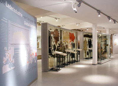 Museumsexposition mit Schautafeln und Vitrinen mit verschiedenen gegerbten Tierhäuten, die Aspekte der Lederindustrie und ihrer weltweiten Verbreitung beleuchten.
